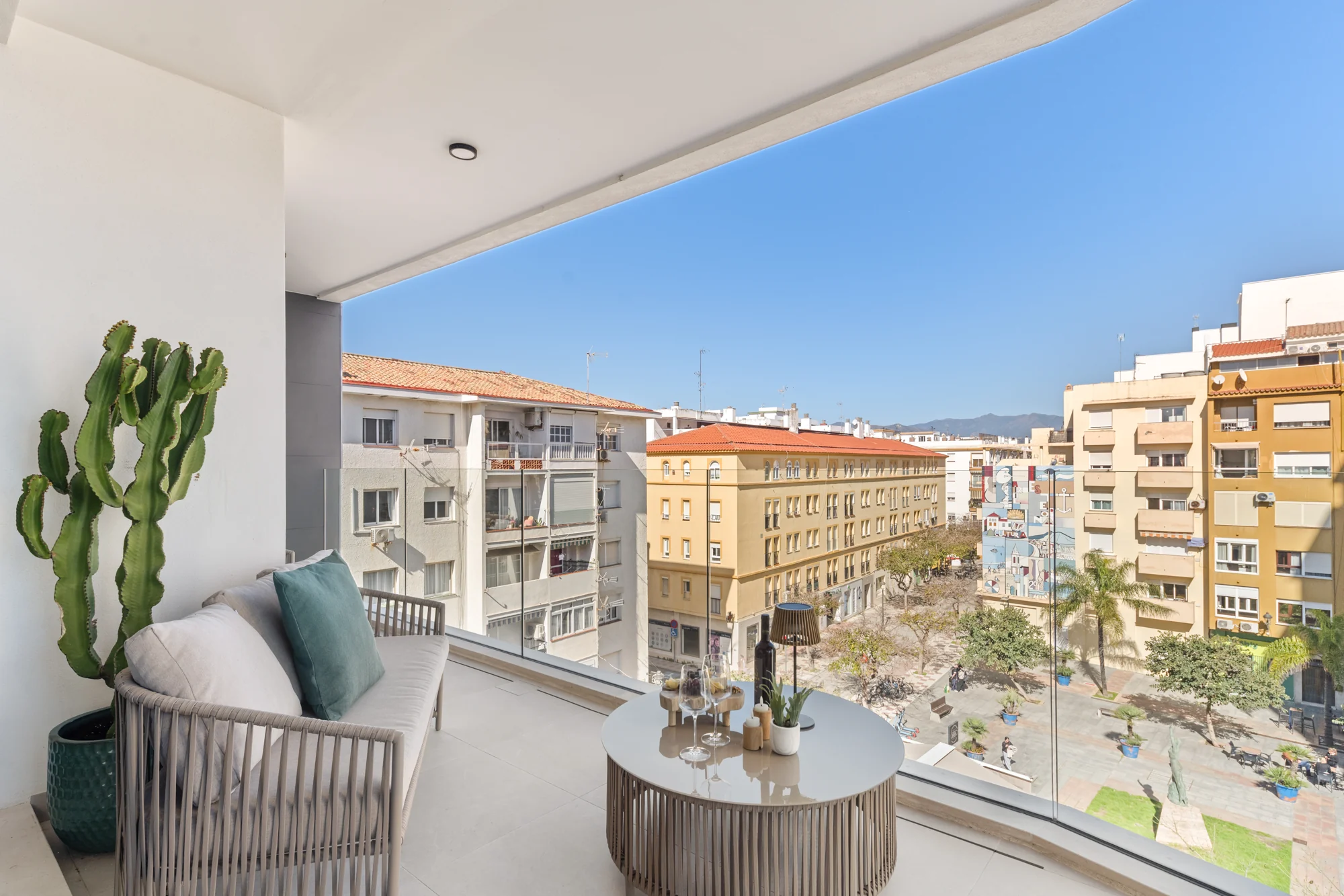 The sunlit terrace with a cactus, lounge chair and table overlooking colourful Plaza ABC in Estepona
