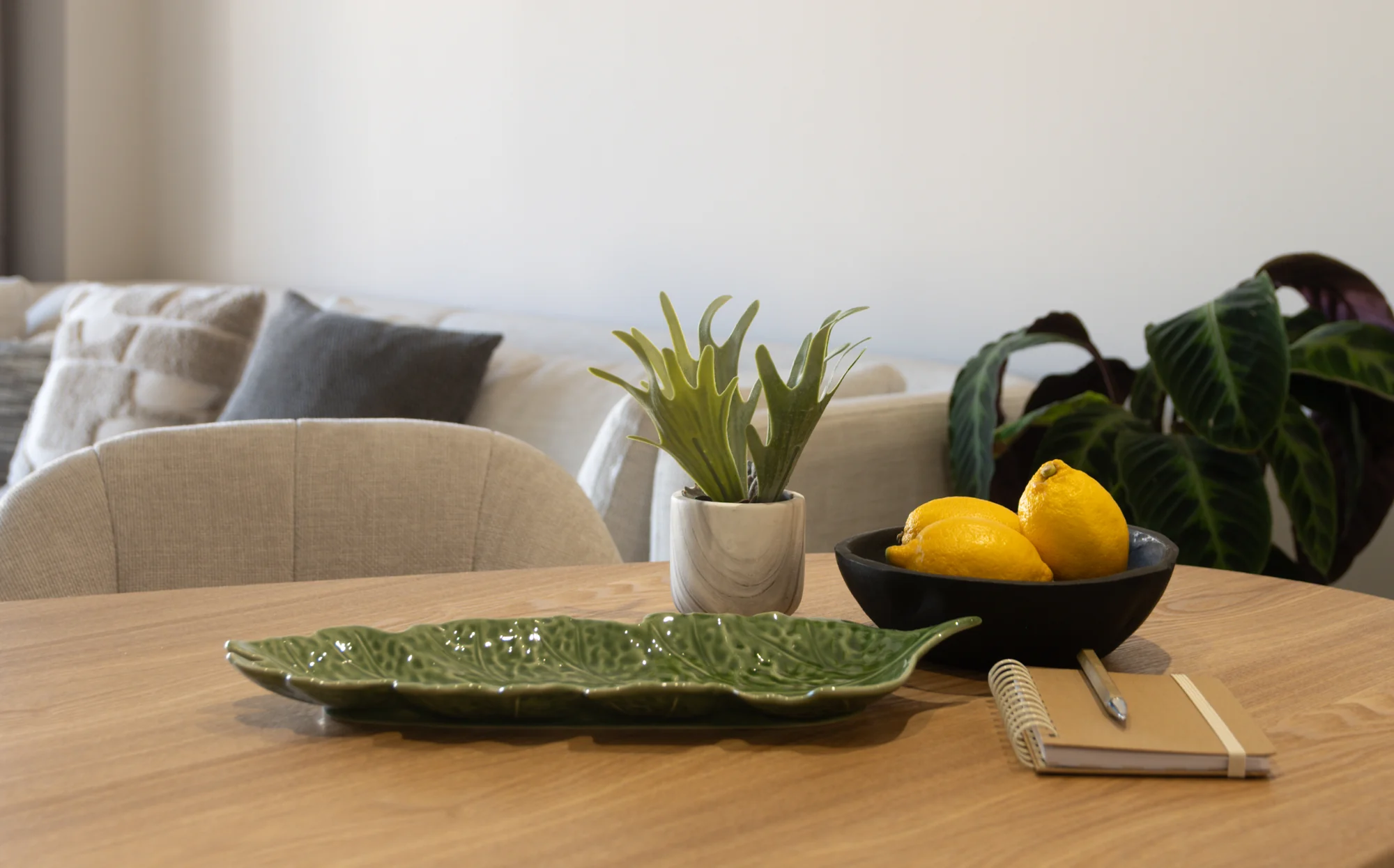 Oak dining table with fresh lemons, a ceramic platter and soft upholstered chairs