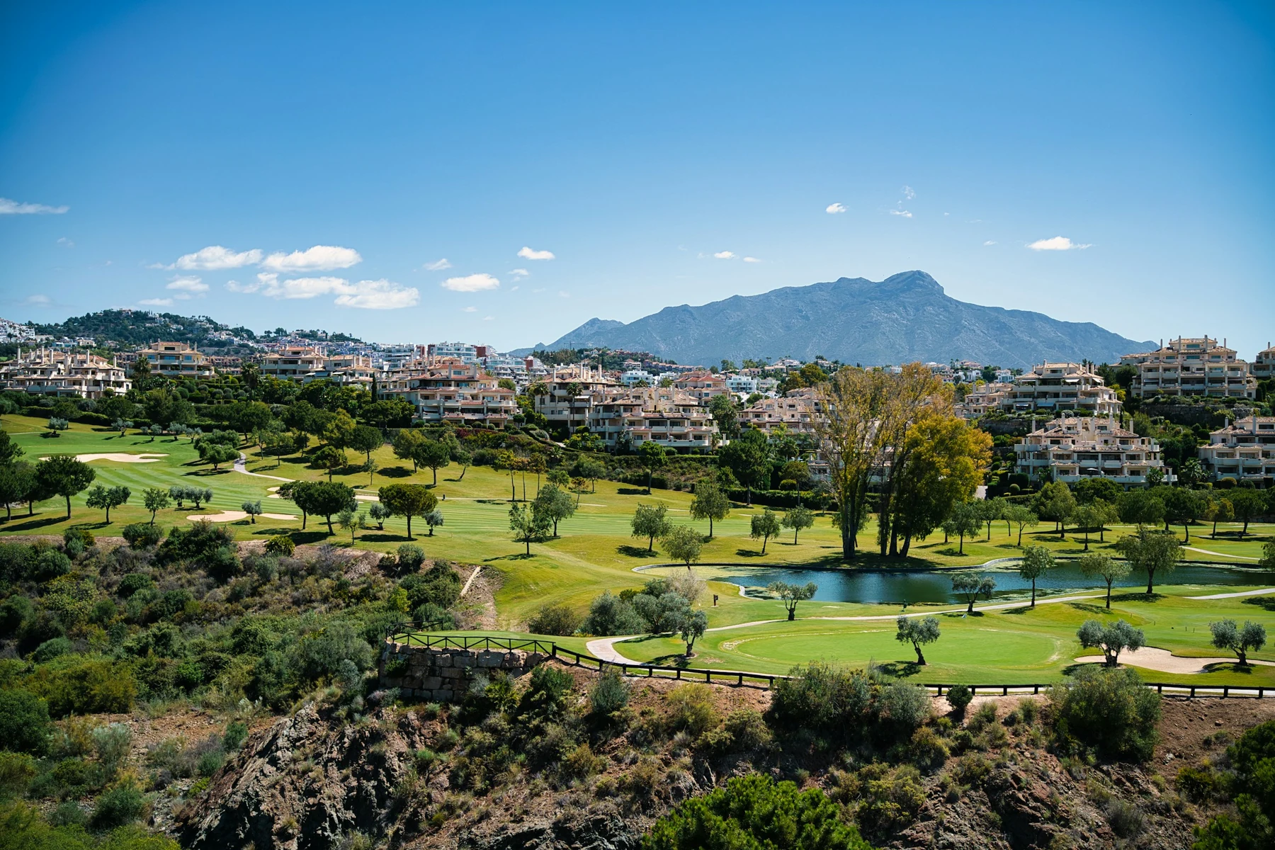 Green fairways, a pond and mountains at a golf course on the Benahavís-Estepona border
